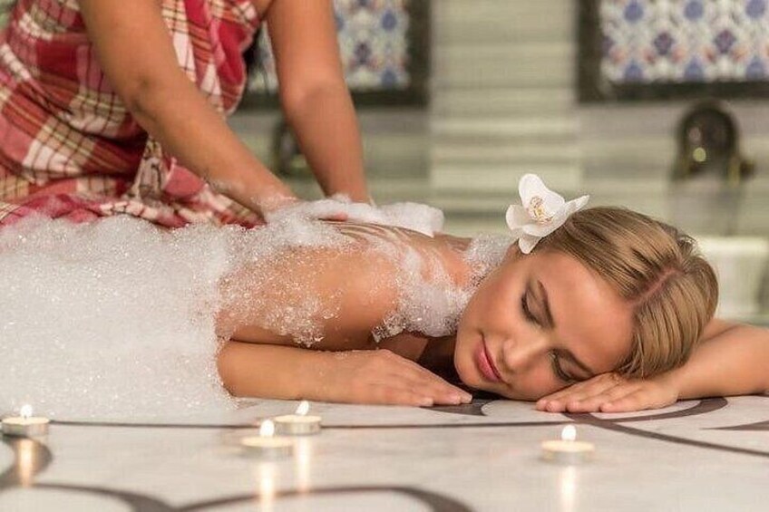 A person receiving a facial treatment with bubbles, candles, and a decorative setting. 1