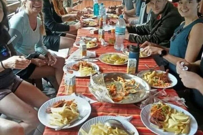 A group of people sitting around a table with plates of food, including what appears to be fried items and salads. 3