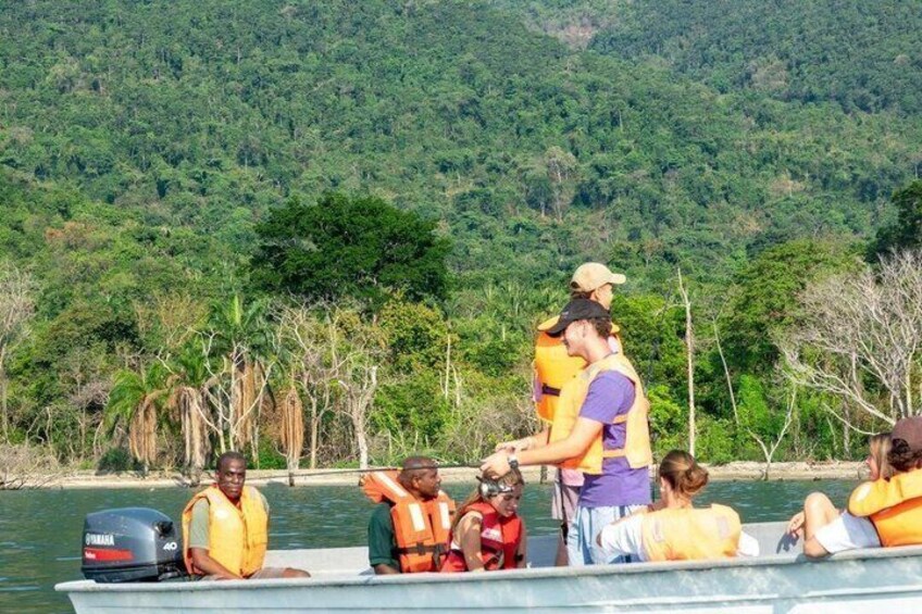 A group of people on a boat with life jackets, surrounded by a forested landscape. 5
