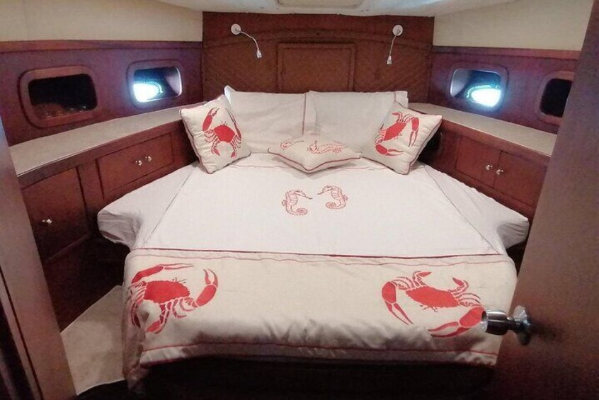 A cabin interior with a bed, wooden cabinets, and two small windows. 2