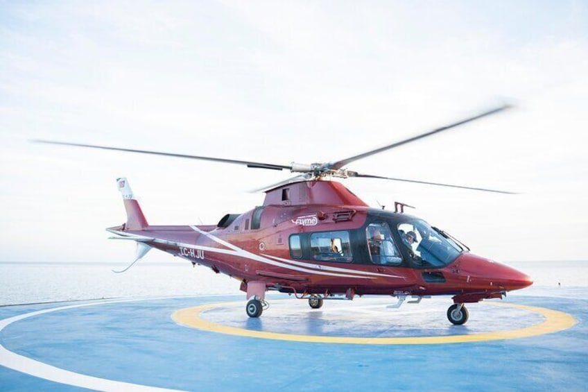 A red helicopter on a blue landing pad with a clear sky in the background. 1