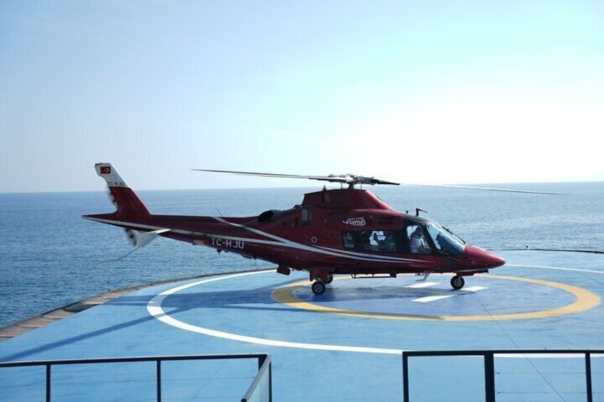 A red helicopter with registration TC-HJU on a helipad near the ocean. 2