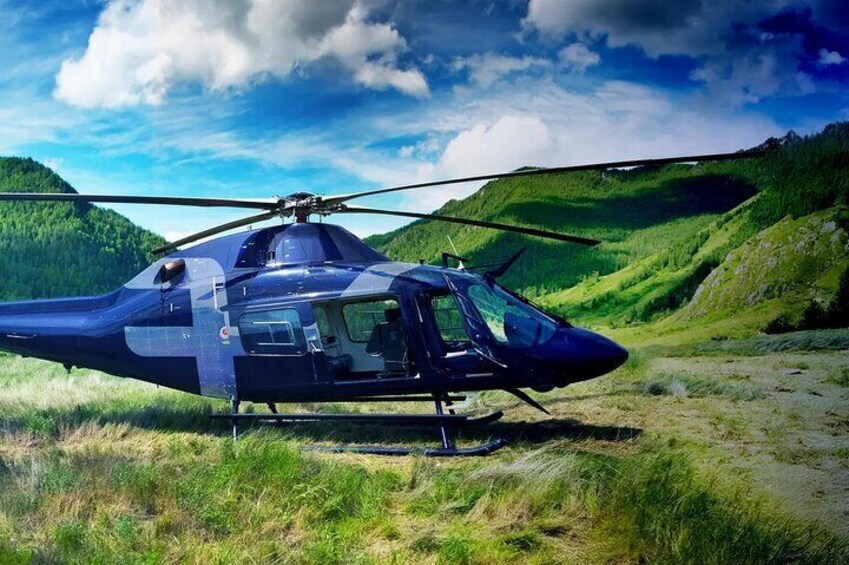 A helicopter parked on a grassy field with a mountainous backdrop. 4
