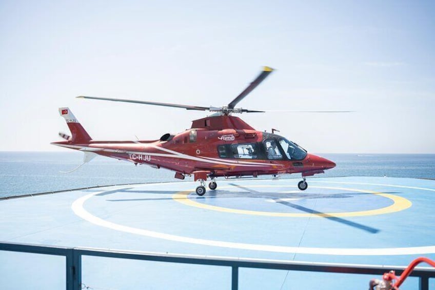 A red helicopter on a helipad with a clear sky and ocean in the background. 5