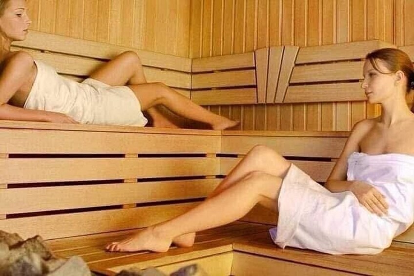 Two individuals in a wooden sauna with benches. 3