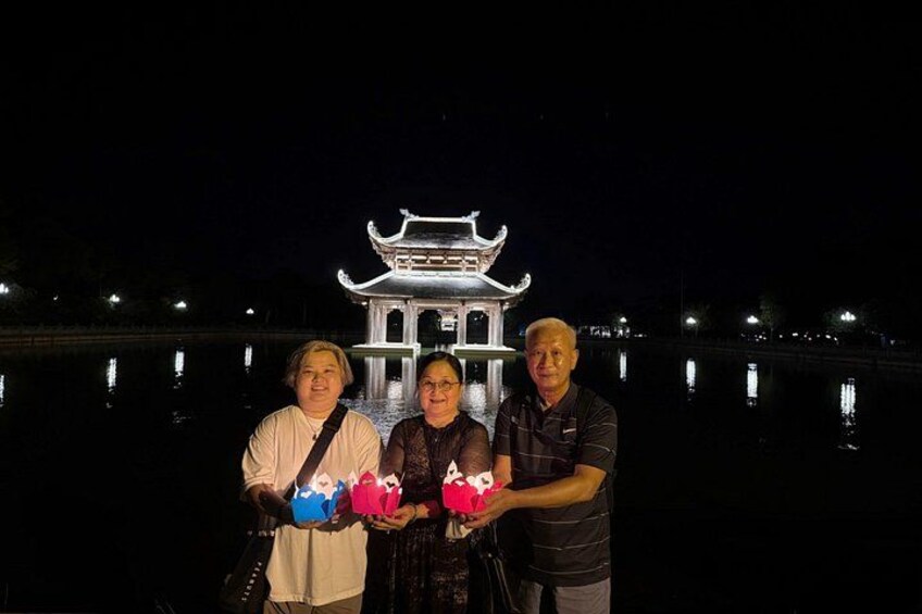 Three people standing in front of a lit-up traditional building by a calm body of water at night. 3