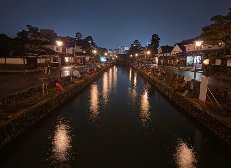 A calm canal at night with houses on either side and lights reflecting on the water. 1
