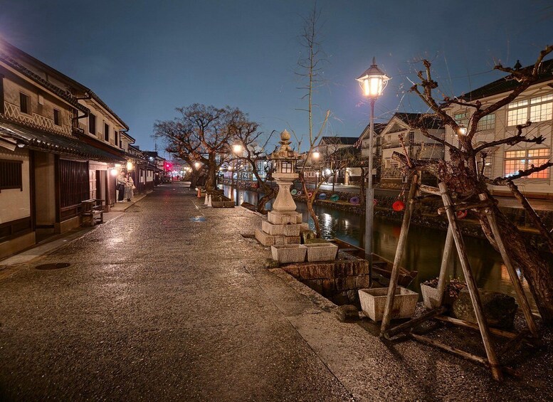 A nighttime street with traditional buildings, a stone lantern, and a river. 4