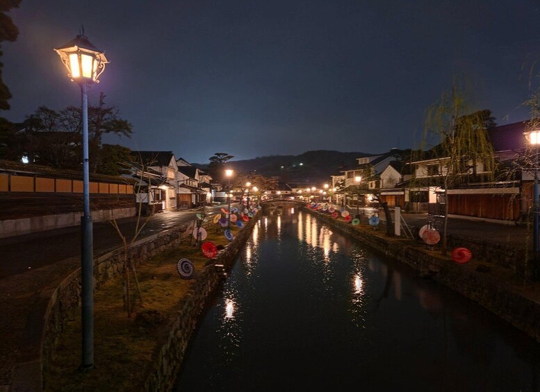 A nighttime riverside scene with traditional buildings, a canal, and decorative umbrellas along the water's edge. 2