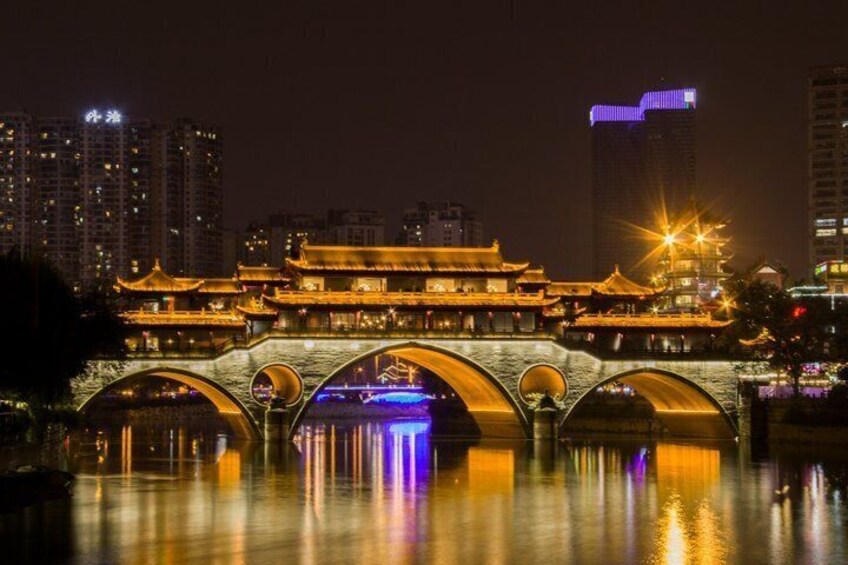 A traditional Chinese bridge with illuminated arches reflecting on the water, surrounded by modern buildings. 2