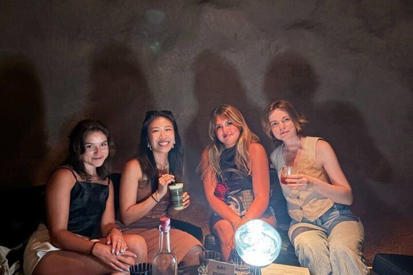 Four people sitting on a couch with drinks, in a dimly lit room. 5