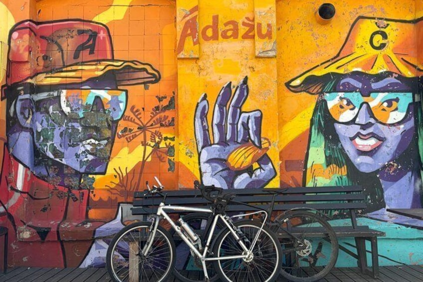 A mural with a bicycle, a bench, and a wall with graffiti. 1