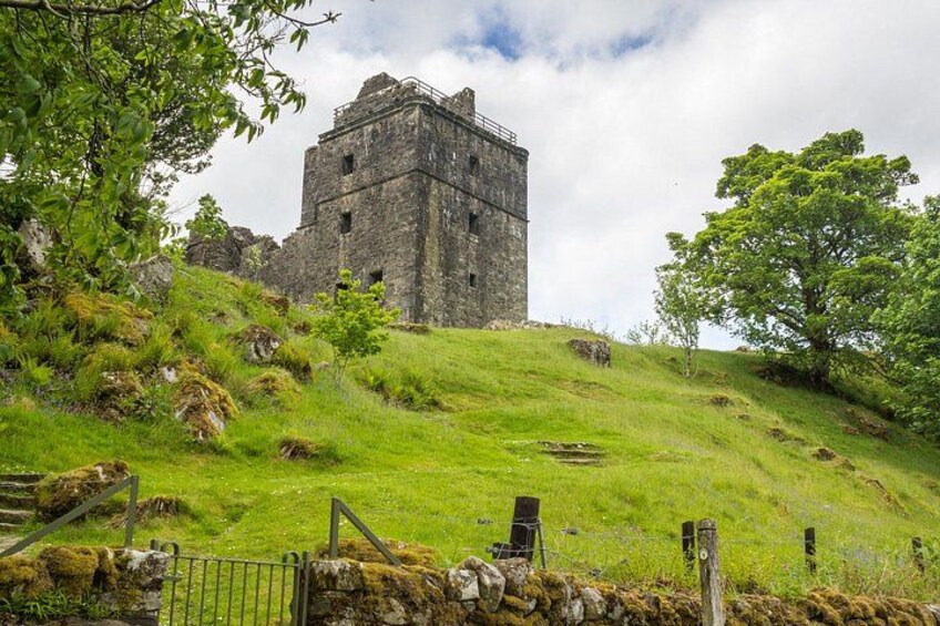 A historic stone tower on a grassy hill with a stone wall and gate in the foreground. 4