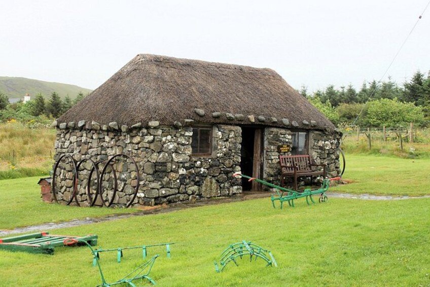 A stone house with a thatched roof, a wooden bench, and a green garden. 2