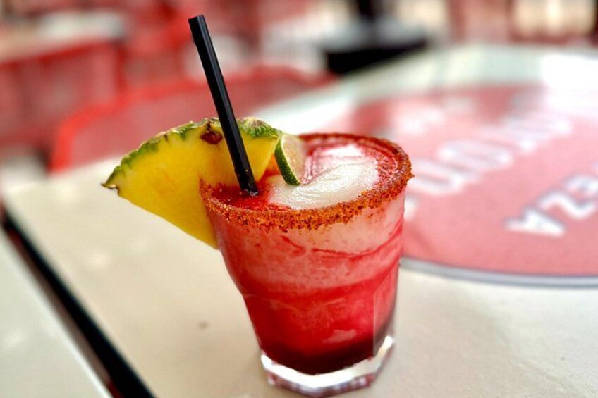 A red cocktail with a pineapple garnish and a black straw, served in a glass with a salted rim. 5