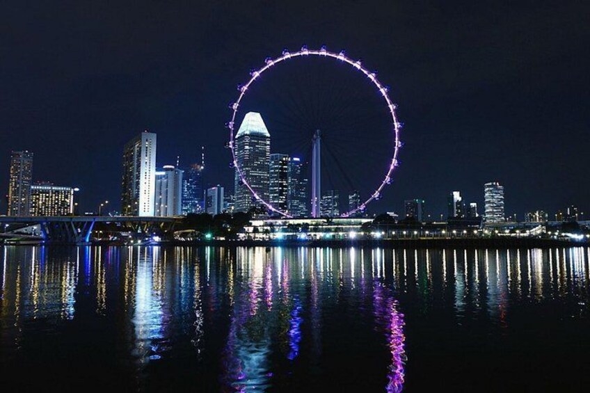 A city skyline at night with a large Ferris wheel reflecting on the water. 3