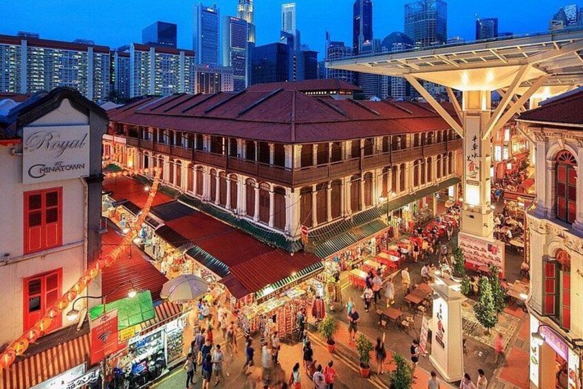 A bustling market street with a historic building, a covered walkway, and a city skyline in the background. 1