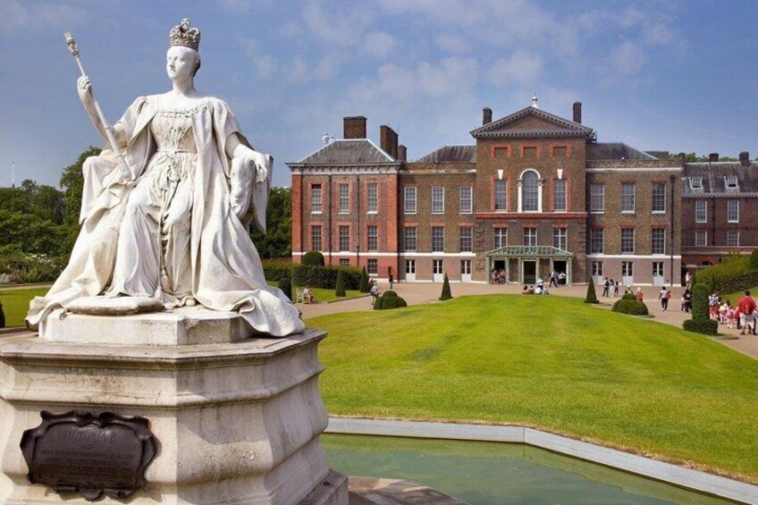 A statue of a crowned figure on a pedestal, a red brick building, and a well-maintained lawn. 4