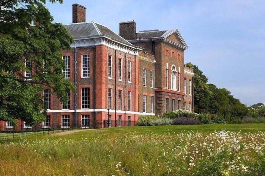 A large brick building with a symmetrical facade, surrounded by a well-maintained lawn and flowering plants. 5