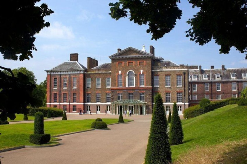 A large brick building with a central entrance, surrounded by well-manicured lawns and trimmed hedges. 1
