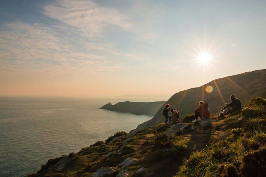 A coastal landscape with people sitting on a grassy hill, overlooking the sea. 5