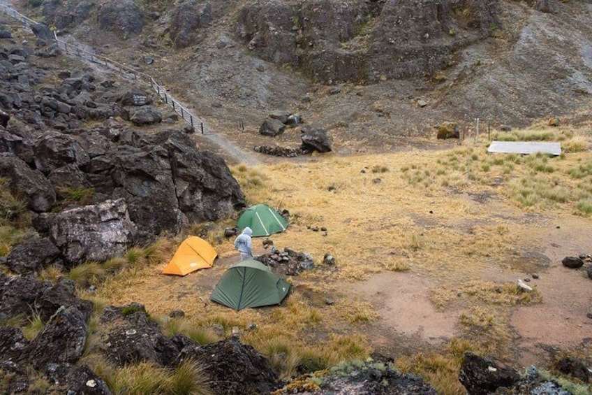 A rocky terrain with three tents and a path. 1
