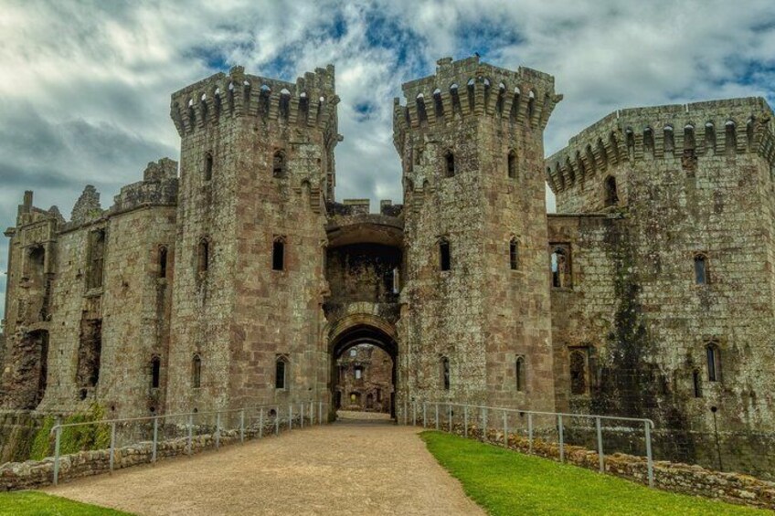A historic castle with two large towers, a central archway, and a gravel pathway leading to the entrance. 3