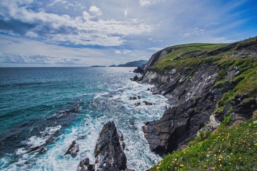A coastal landscape with rocky cliffs, a clear blue sea, and a grassy hill. 3