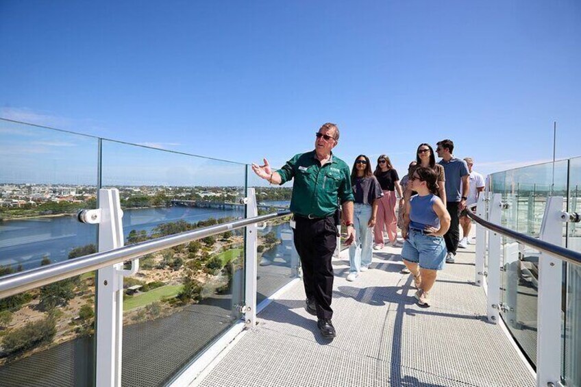 A group of people walking on a glass bridge with a river and cityscape in the background. 2