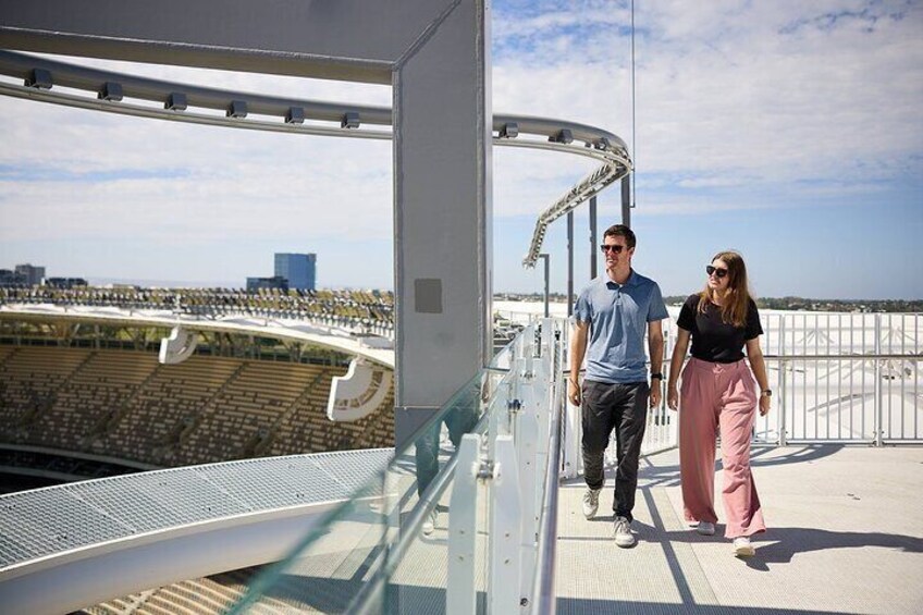 A couple walking on a bridge with a stadium in the background. 4