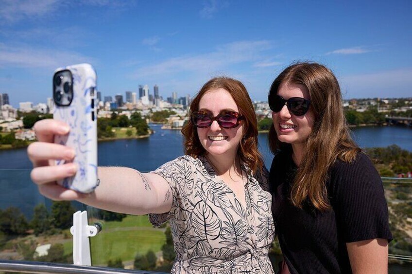 Two people taking a selfie with a cityscape and river in the background. 3