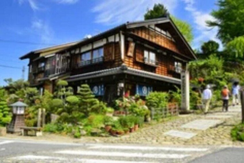 A traditional wooden house with a steeply pitched roof, surrounded by lush greenery and a stone pathway. 2