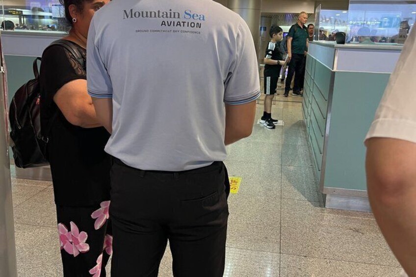 A person wearing a 'Mountain Sea Aviation' shirt, standing in an airport terminal. 2
