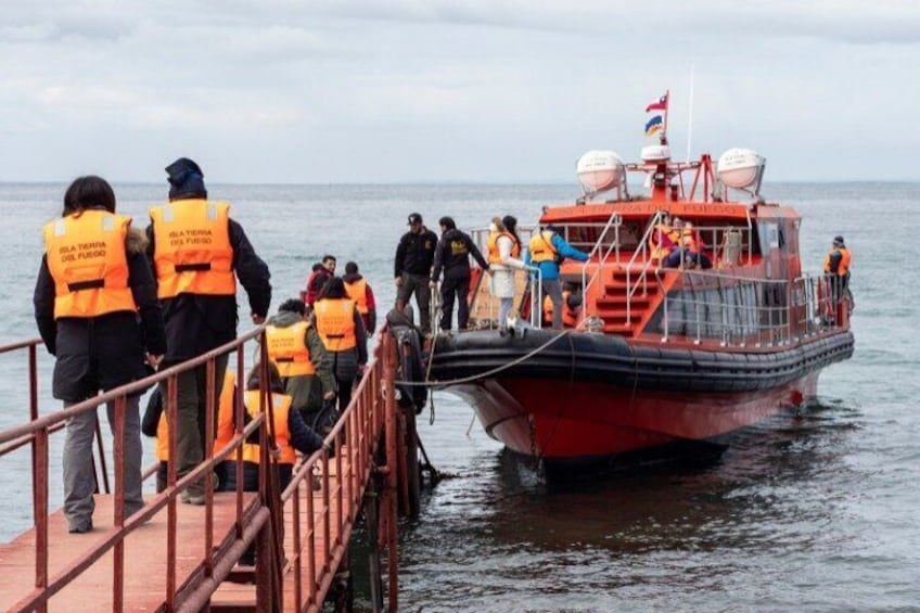 A red boat with people wearing orange life jackets on a dock. 3