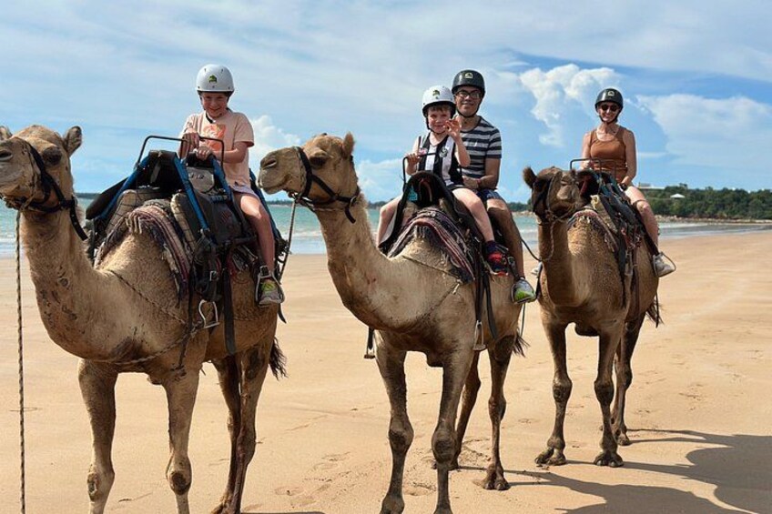 Three people riding camels on a sandy beach with the ocean in the background. 3