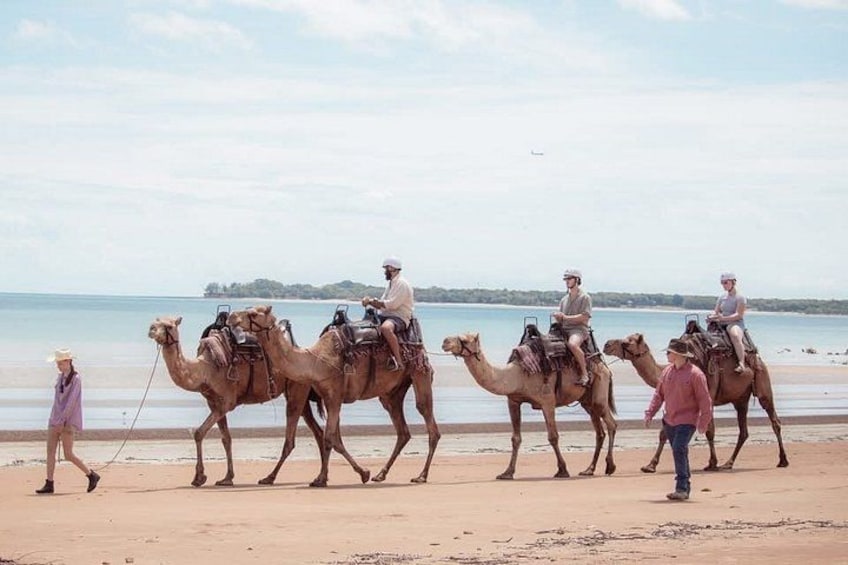 A group of people riding camels on a beach with the ocean in the background. 1