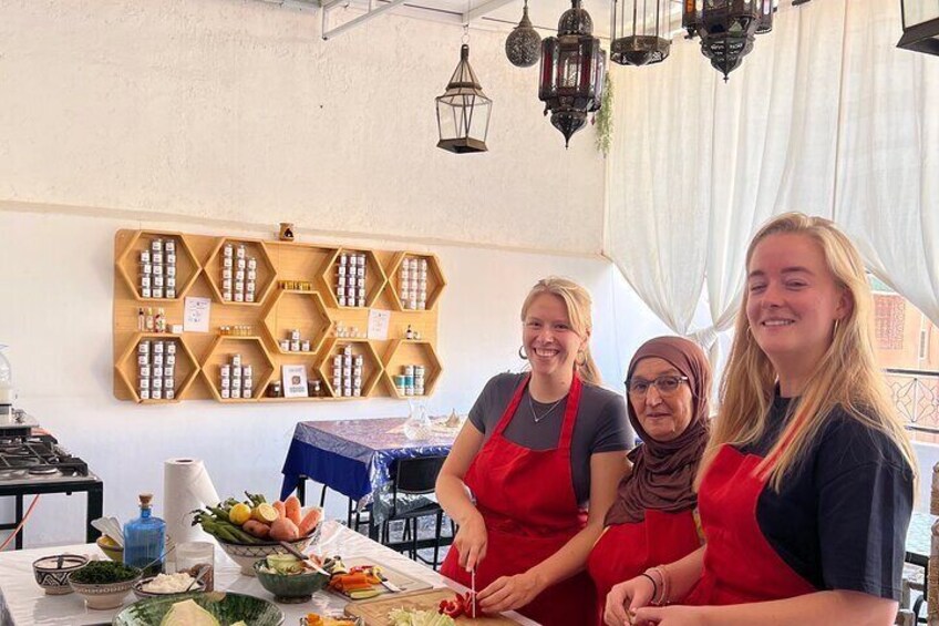Three people in aprons at a table with food and a hexagonal spice rack in the background. 1