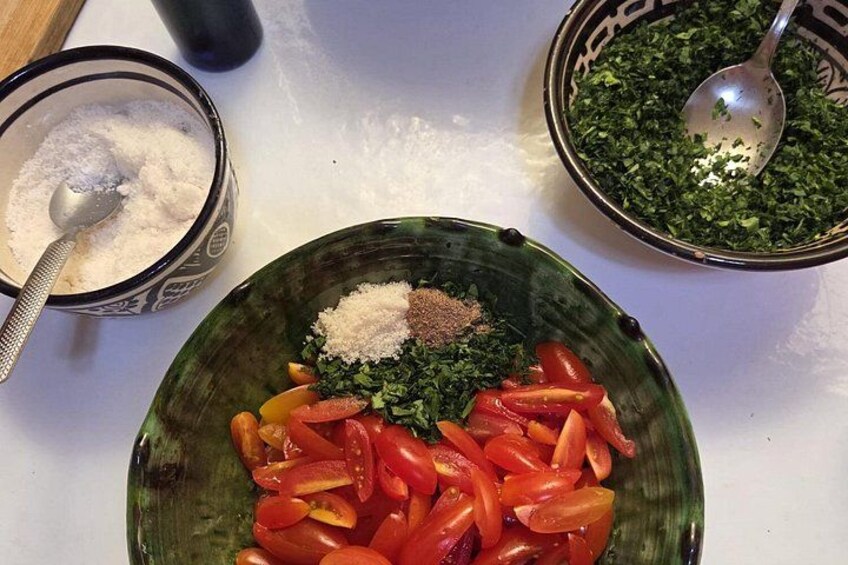 A bowl of chopped tomatoes, a bowl of chopped herbs, and a bowl of salt and pepper on a kitchen counter. 5