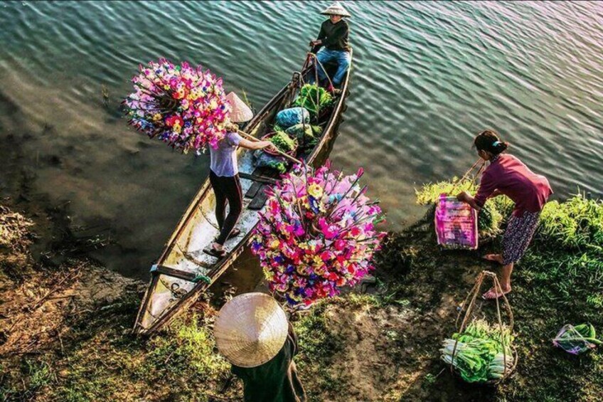 People on a boat carrying colorful flower bouquets, and another person collecting plants near the shore. 4