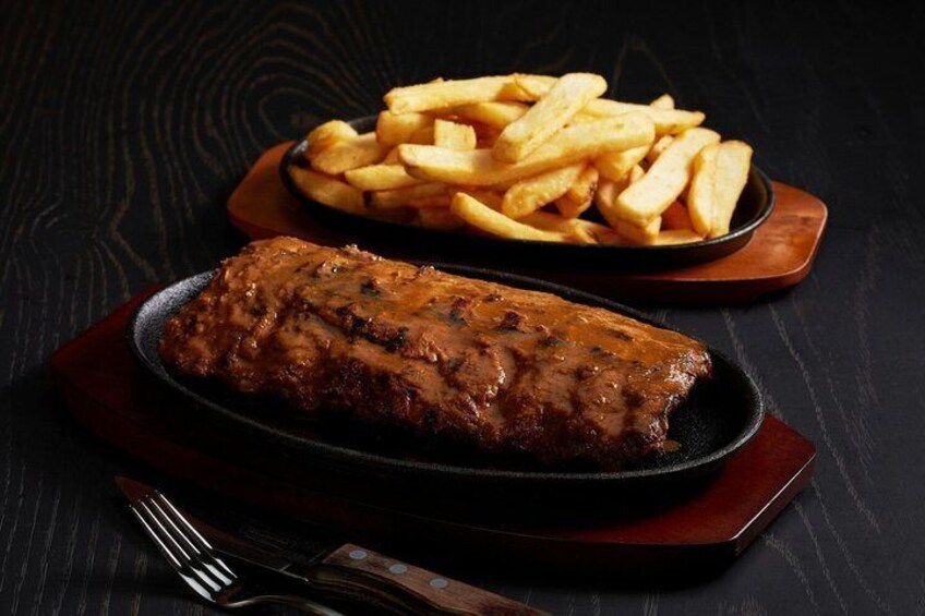 A grilled meat dish and a plate of French fries on a dark wooden table. 2