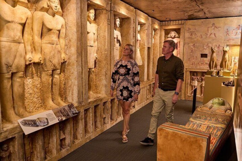 A museum interior with ancient Egyptian statues and sarcophagi on display. 1