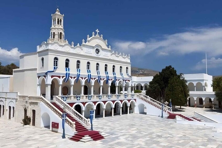 A white church with a bell tower, red and blue staircases, and a tiled courtyard. 4