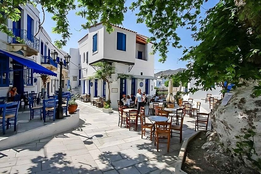 A sunny street with outdoor seating, blue awnings, and white buildings. 5