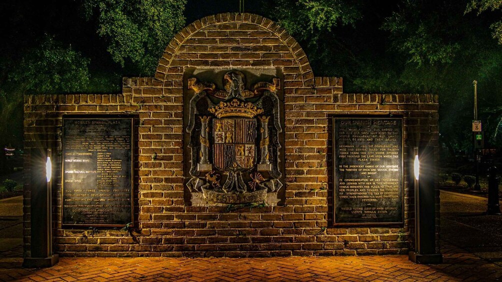 A brick monument with a coat of arms and two plaques with text. 4