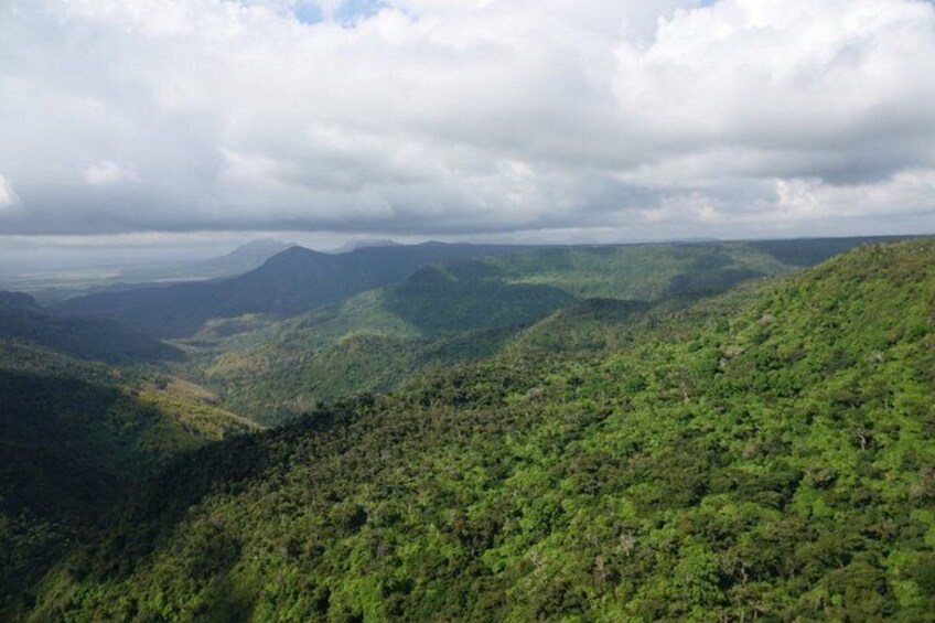 A mountainous landscape with dense green forests and a cloudy sky. 1