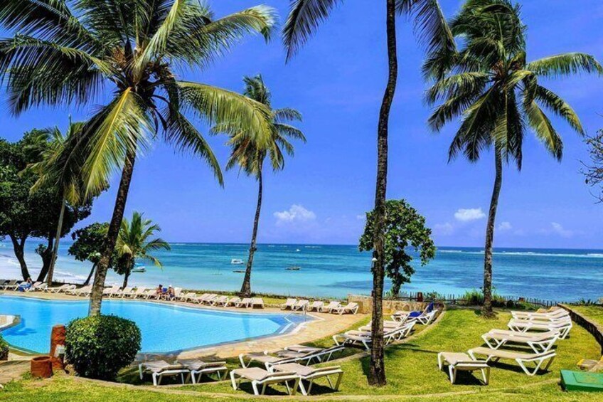 A poolside with lounge chairs, palm trees, and a clear blue ocean. 2