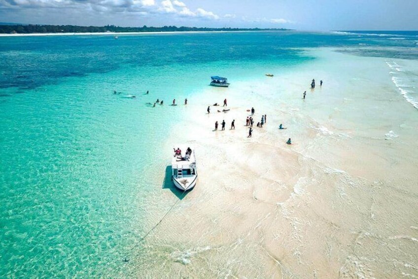 A beach with clear turquoise water, a boat, and people on the shore. 5