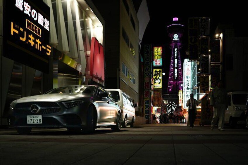 A nighttime urban street with illuminated signs and a parked car. 5
