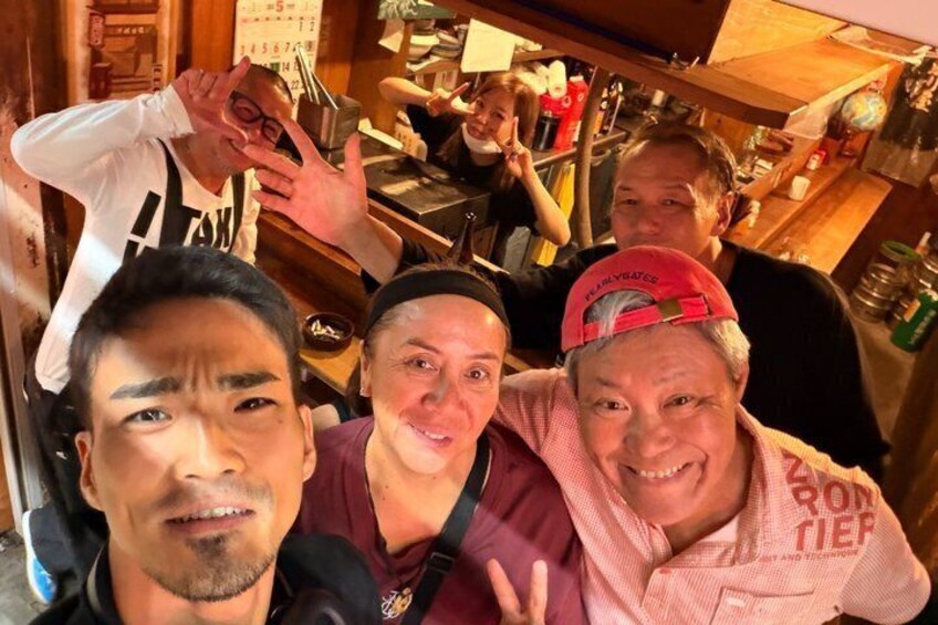 A group of people in a bar setting with wooden furniture and various bottles in the background. 4