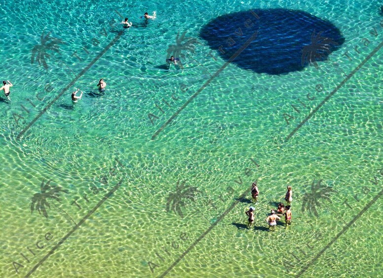 A clear blue sea with people swimming and standing in shallow water. 3